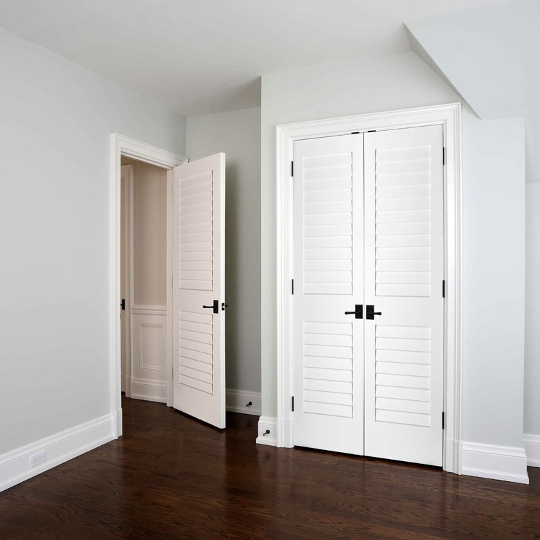 A white louvered bedroom door in a room with wood floors and white louvered closet doors