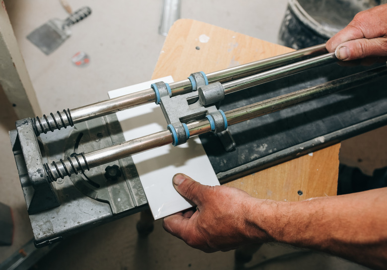 Tile cutter in the man's hand. A builder is cutting white tiles for renovation maintenance work indoors.