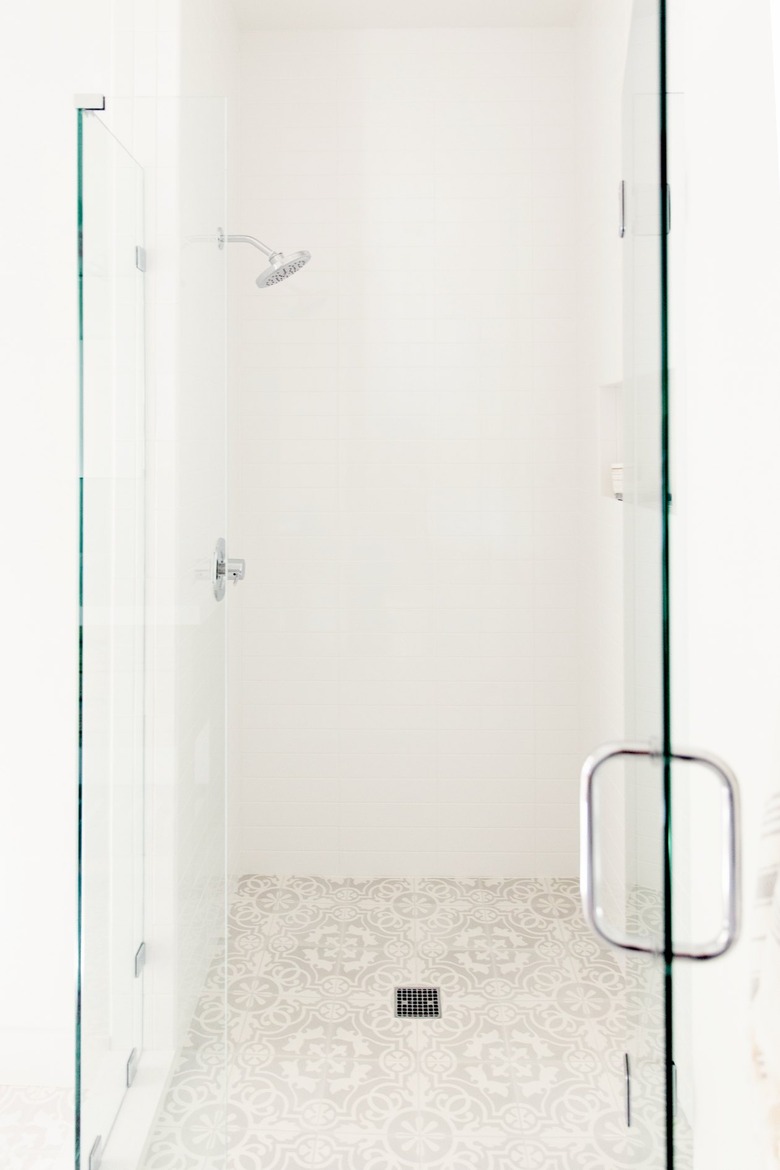 A glass shower door with a chrome handle in a white bathroom. Behind it