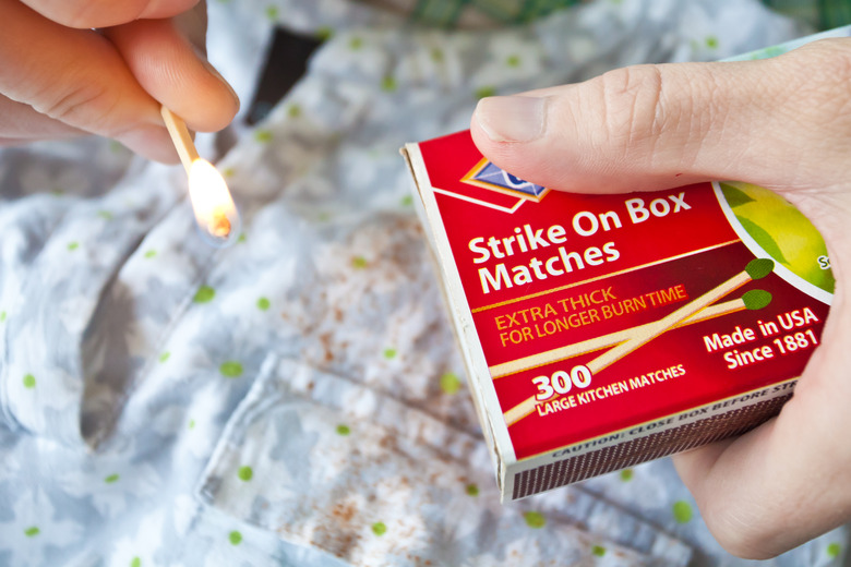 A person holding matches over a piece of fabric