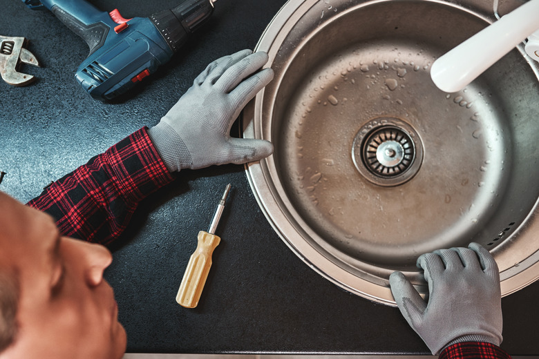Inside view. Close-up of handsome plumber repairing sink in kitchen