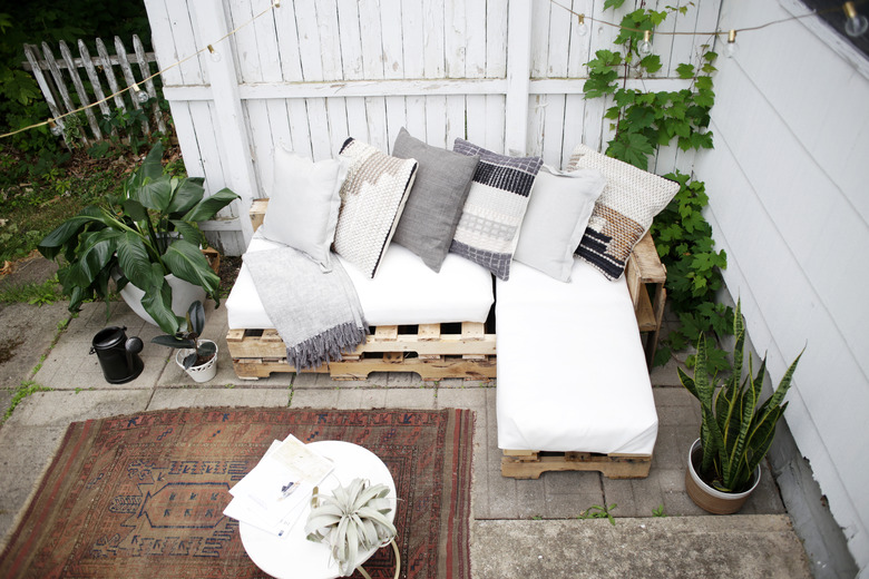 Wood pallet couch on patio with white cushions and throw pillows.