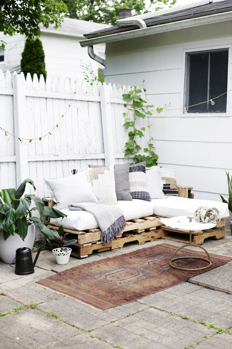 Wood pallet couch on patio with white cushions and throw pillows.