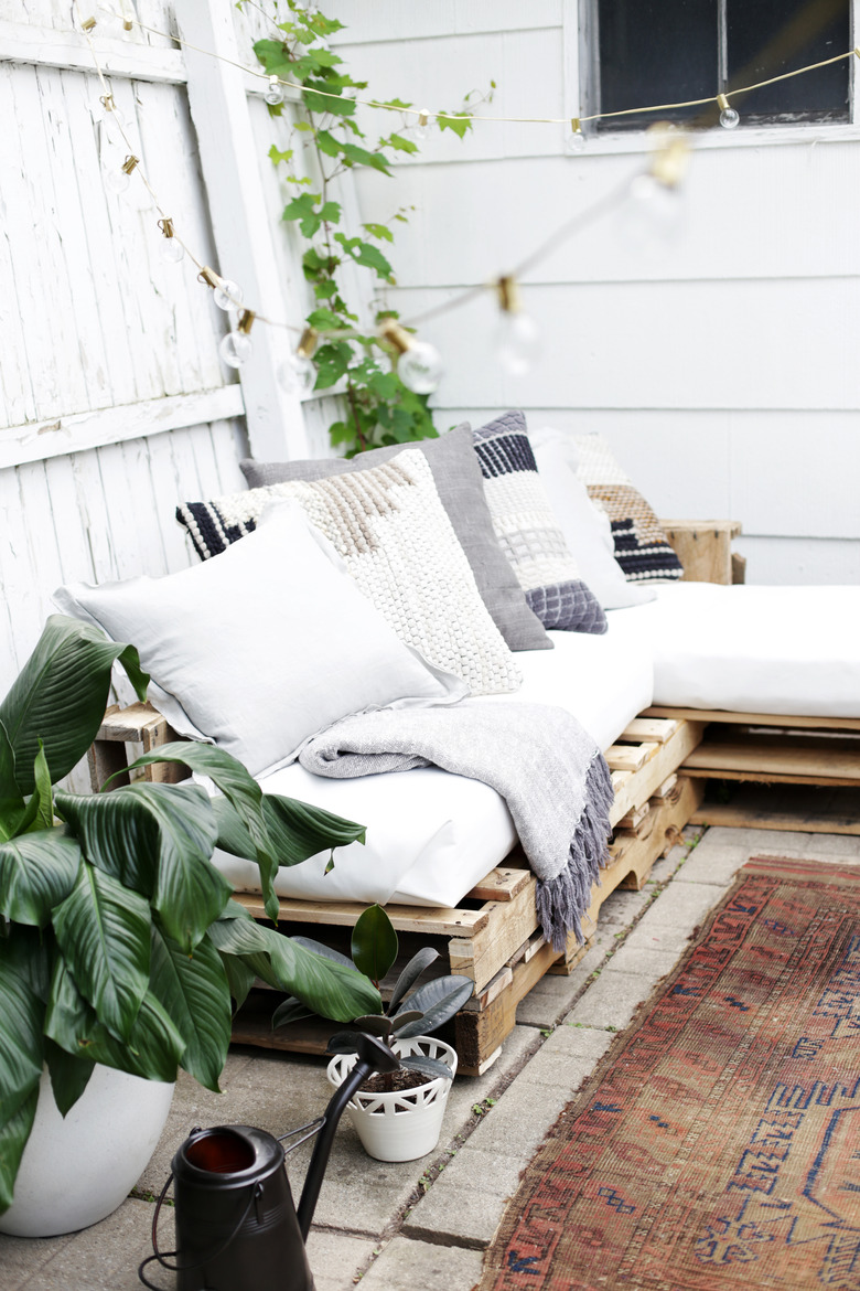 Wood pallet couch on patio with white cushions and throw pillows.