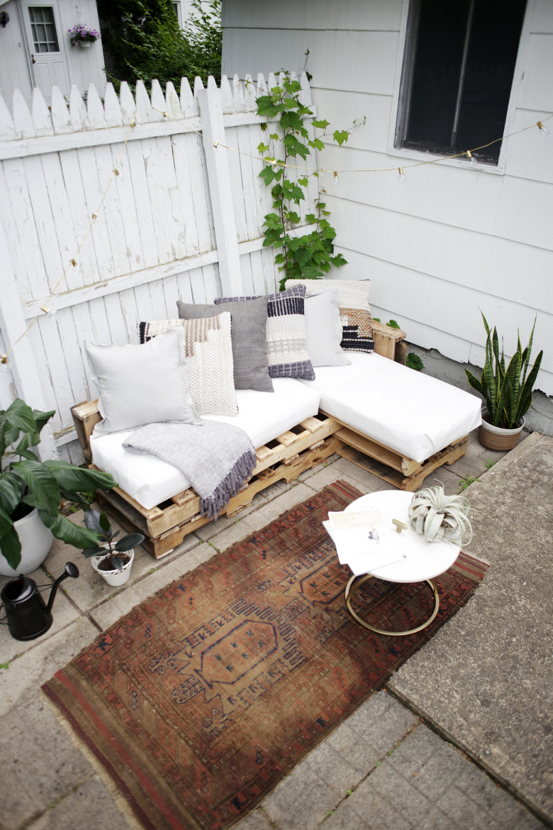 Wood pallet couch on patio with white cushions and throw pillows.