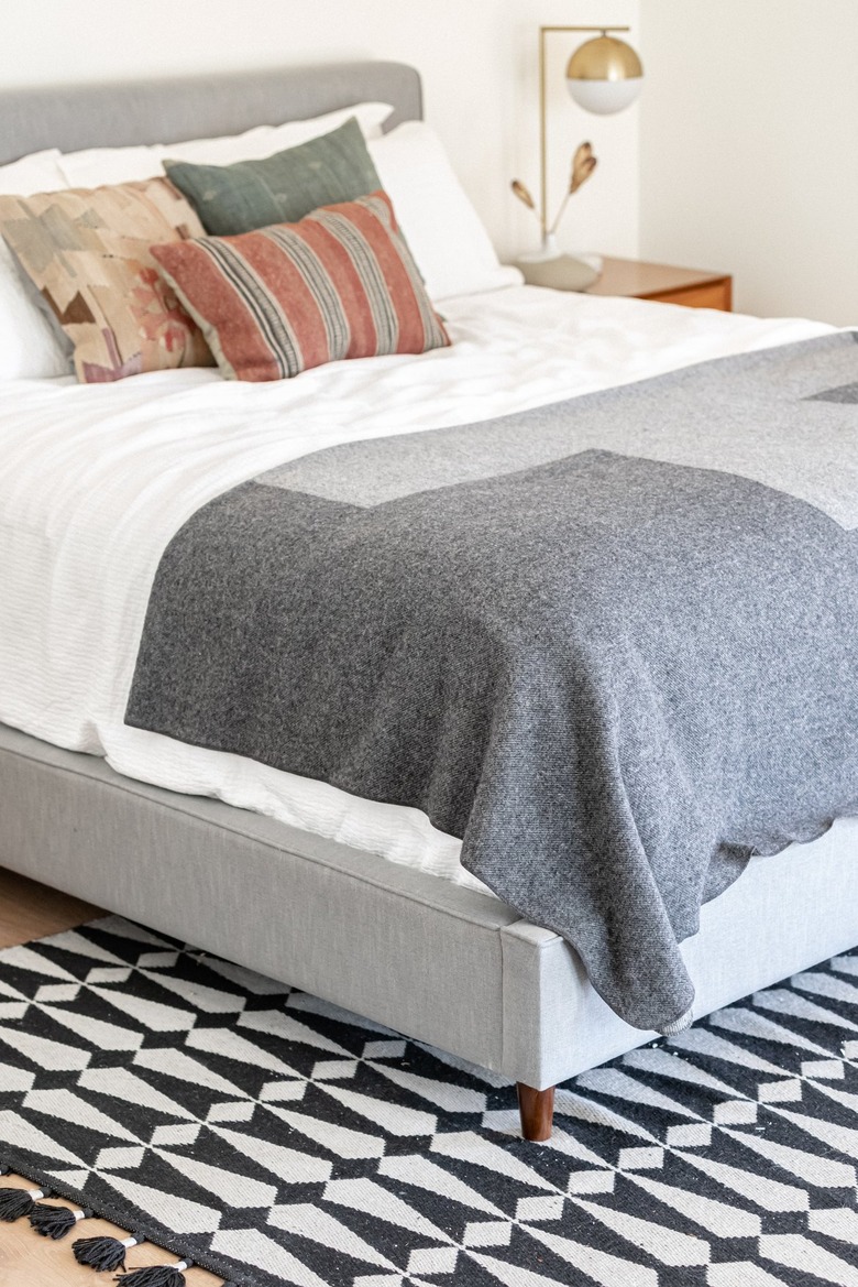 A white frame bed with gray-white bedding and a bold black-and-white patterned rug