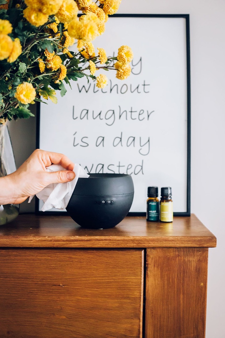 Hand using sanitary sheet to wipe black essential oils diffuser and yellow flowers