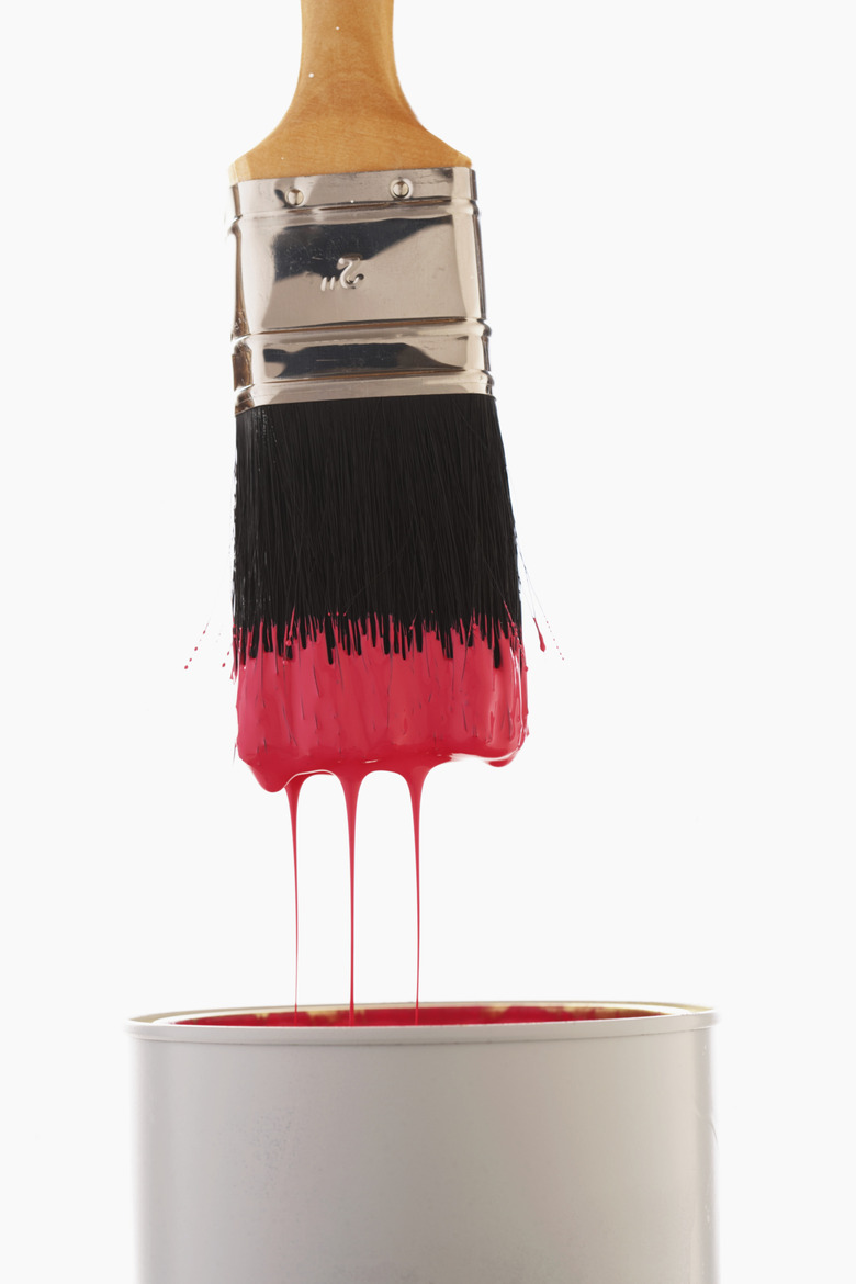 Paintbrush dripping red paint into paint can