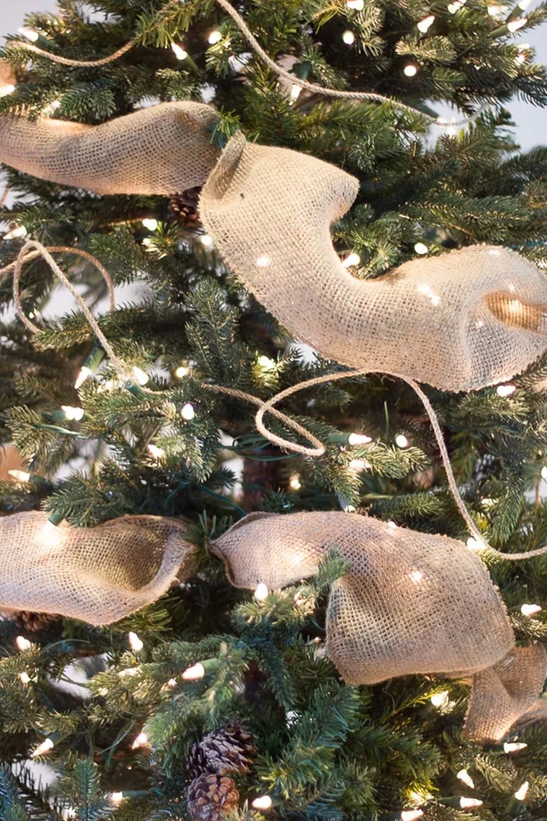A skinny ribbon garland and a larger burlap ribbon are wrapped around a Christmas tree