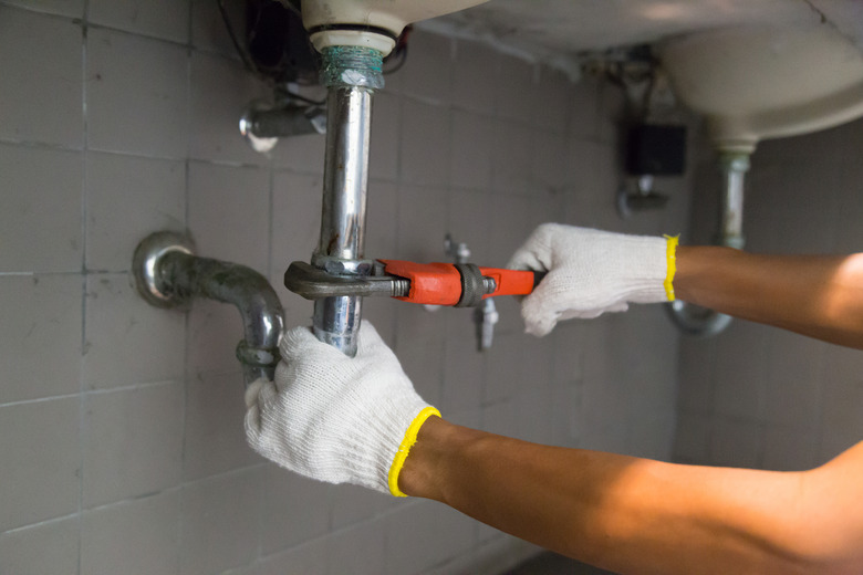 Plumber fixing white sink pipe with adjustable wrench.