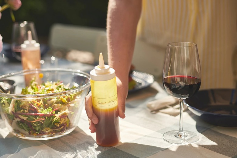 person holding squeeze bottle on table near salad bowl and wine glass