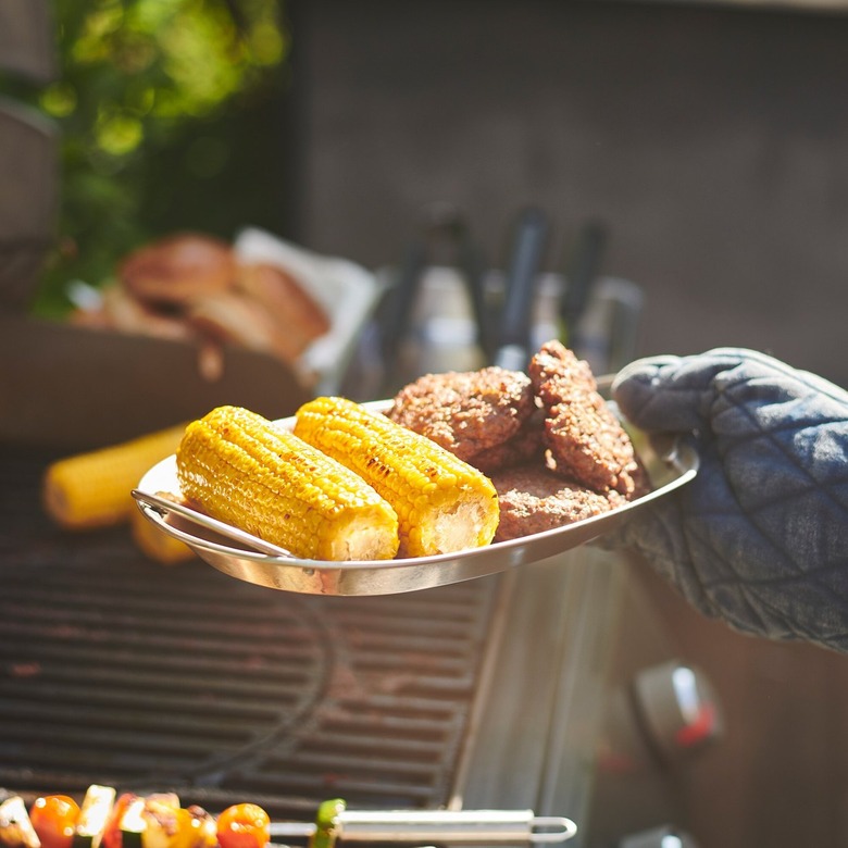 person holding a tray with corn and fried food near grill