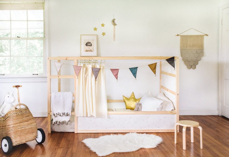 a kura bed frame that has been hacked by adding curtains and bunting and decorating surfaces with wallpaper