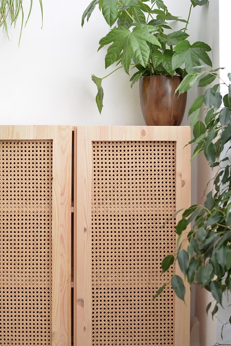 Plywood cabinet with cane paneling in a white room with vined potted plant resting on top of cabinet