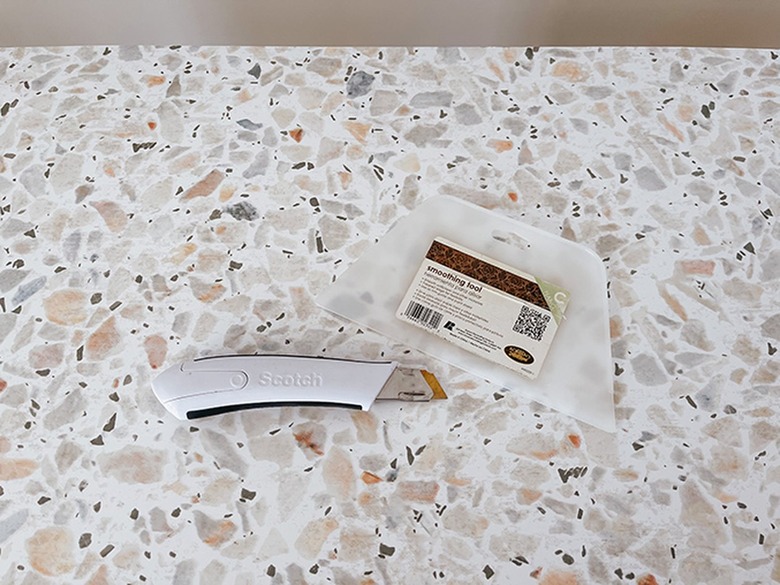 Use a sharp utility knife and wallpaper smoothing tool to adhere the wallpaper to the shelf.