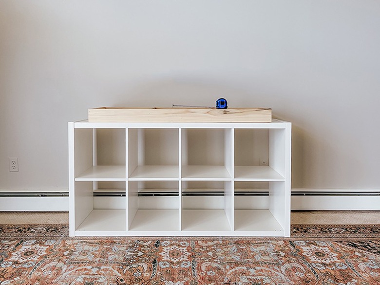 Center the wooden base on the bottom of the IKEA Kallax shelf.