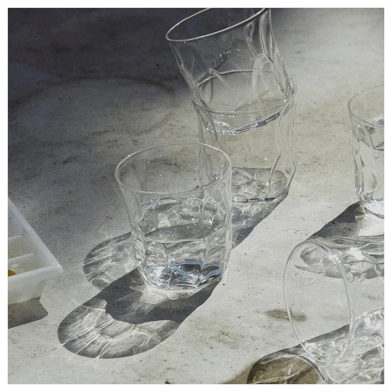 Several clear rippled short drinking glasses on a light gray surface featuring sunlight reflections.
