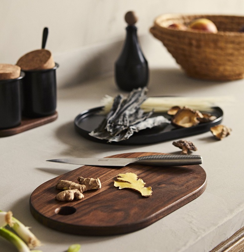 Wooden cutting board with knife and ginger on a countertop with other plates