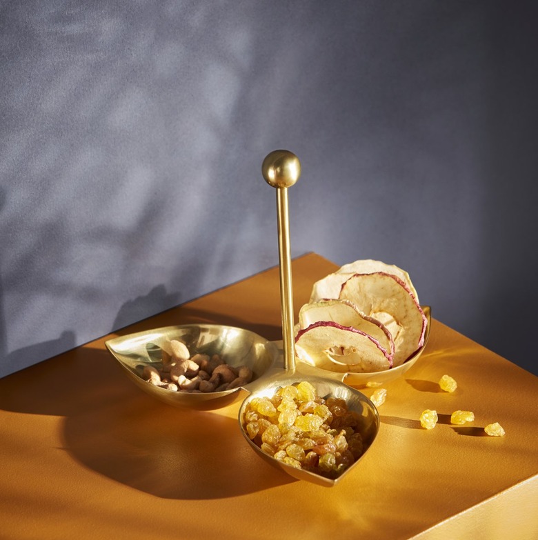 A tray separated into three leaf shapes full of spices on a brown tabletop with a gray wall.