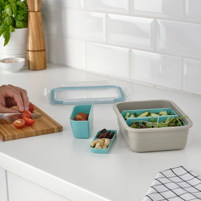 lunch box with containers on counter near hand chopping vegetables on a cutting board