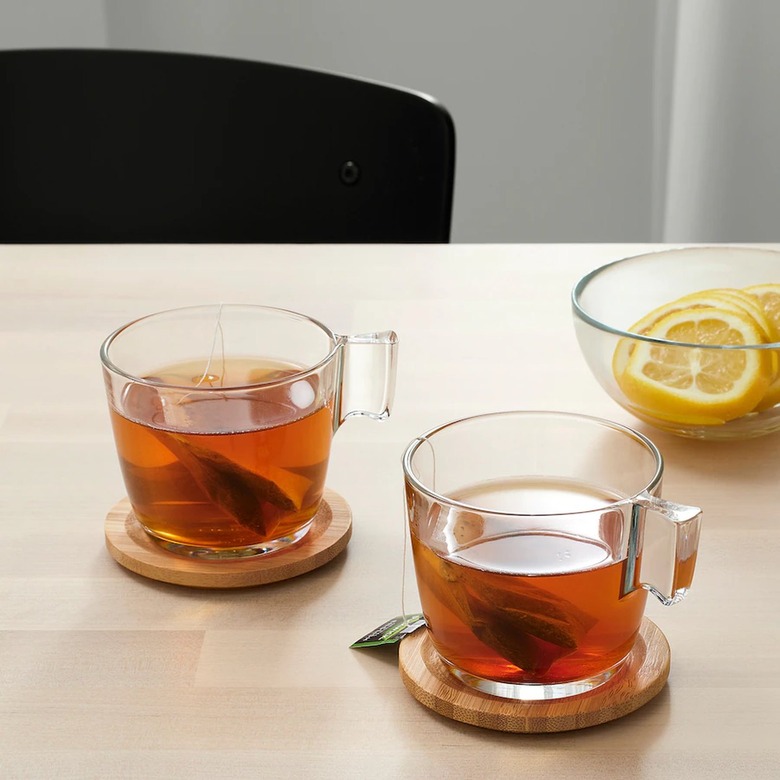 two clear mugs with tea on coasters and bowl with lemons nearby