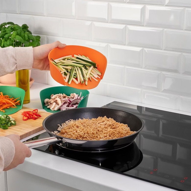 A hand pours veggies into a frying pan