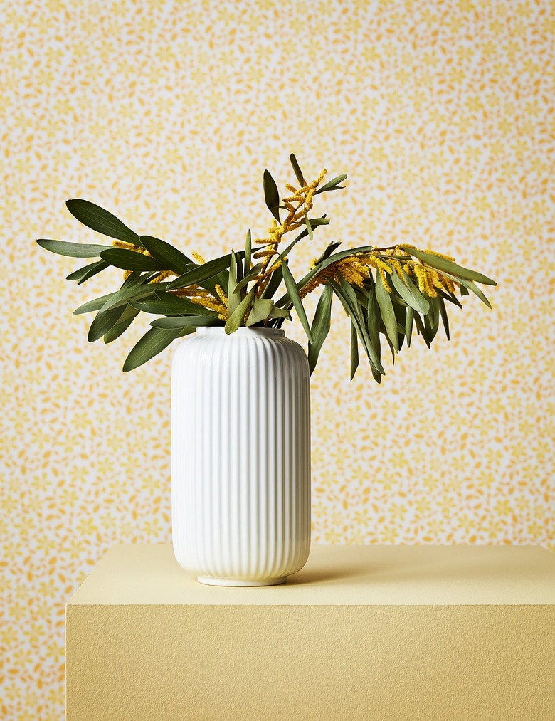 white fluted vase with plant on yellow table with yellow patterned wall in the background