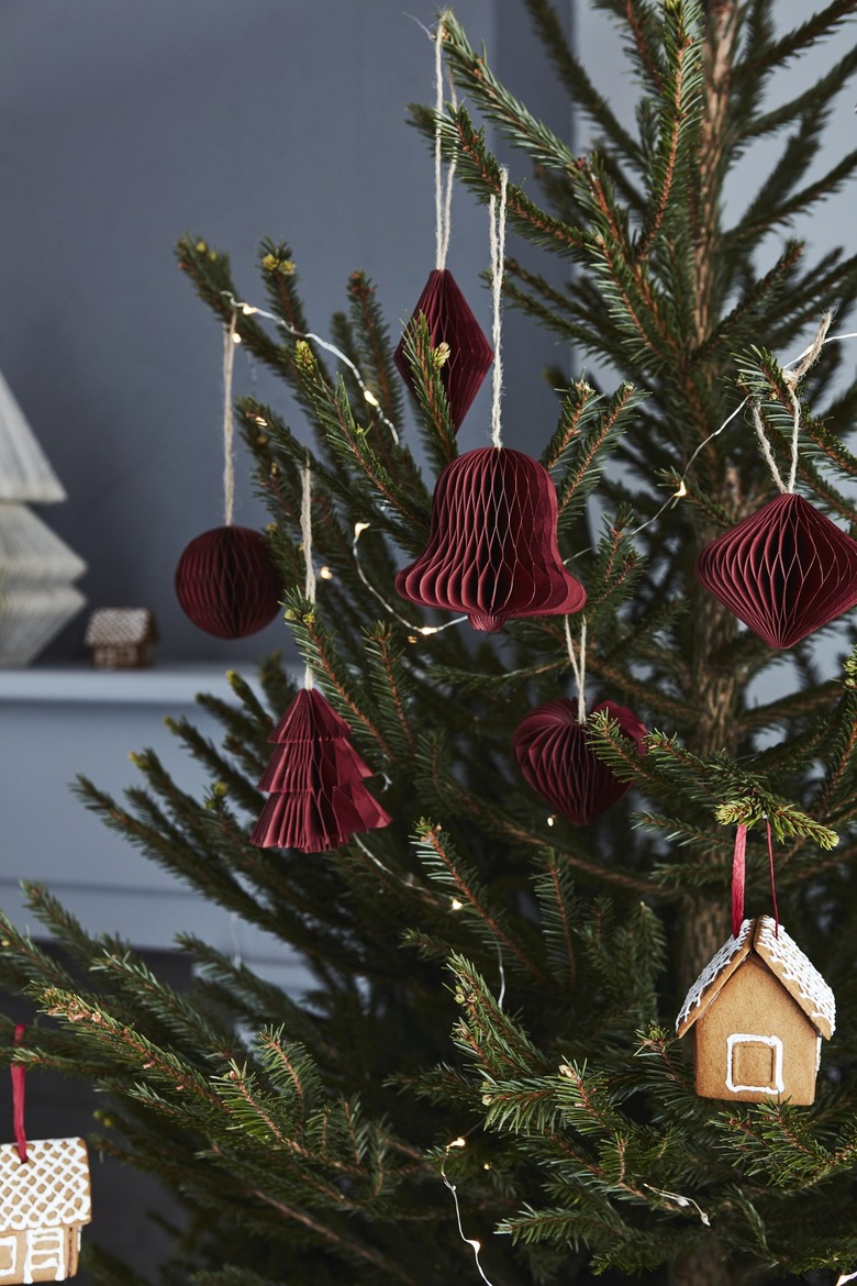 Red paper bell ornaments decorating a Christmas tree in front of a blue wall.