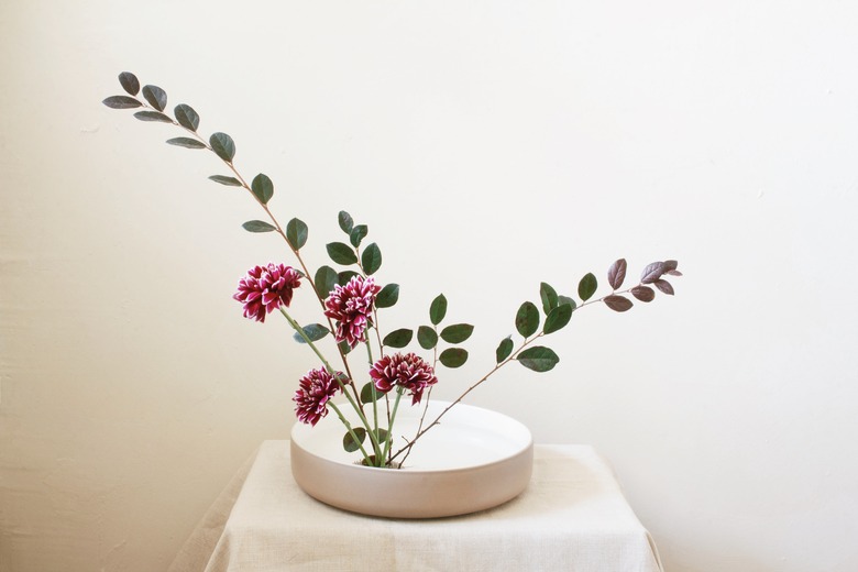 burgundy flowers and leaf stems inserted into flower frog inside shallow bowl