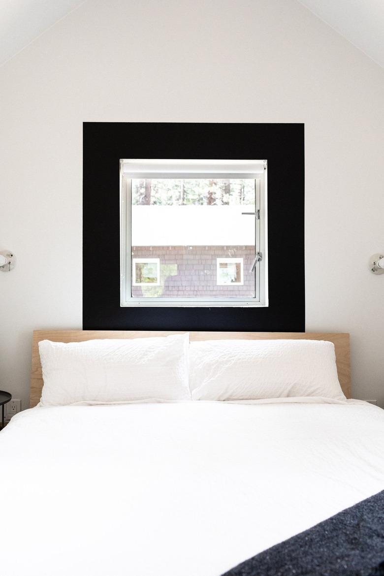 A minimalist white bedroom with a black framed window