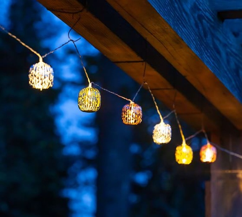 mixed-metal string lights hanging from a wood beam outside at dusk