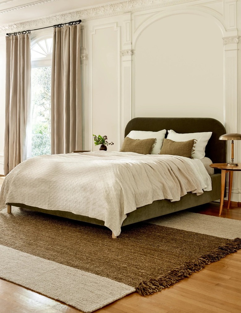 A beige rug with a brown stripe through the center beneath a bed with white and beige linens.