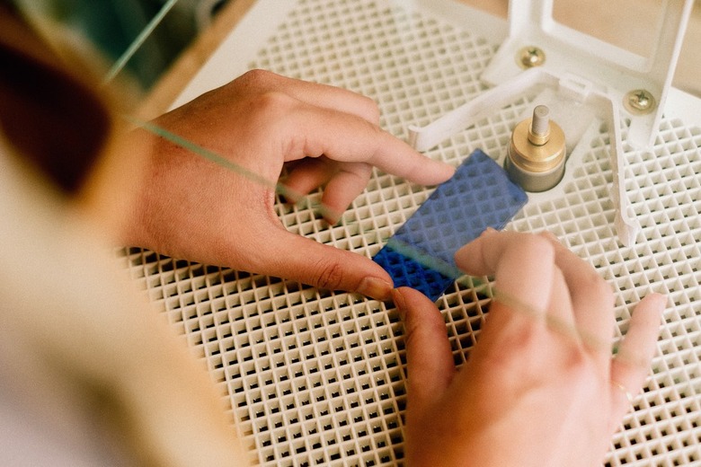 hands below clear glass grinding a small rectangular piece of blue glass on a white grille