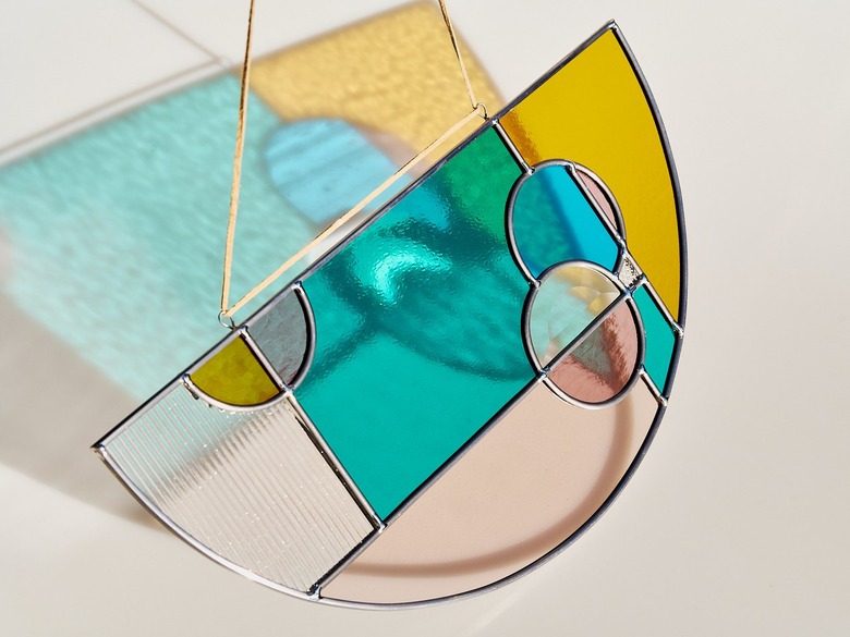 Half-circle stained glass piece with circles and rectangles overlapping in various colors with hanging cord and a reflecting shadow