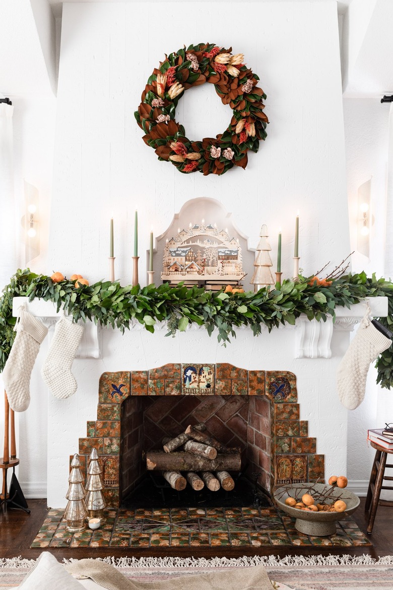 An evergreen wreath over a white fireplace with a lush green garland