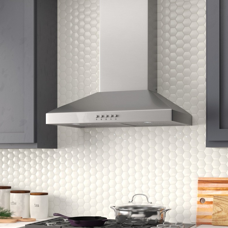 A stainless steel wall-chimney vent hood in a kitchen with a white circular backsplash and gray painted cabinets