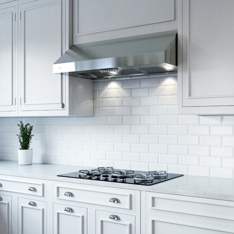 A stainless steel undercabinet vent hood in a white kitchen with a subway tile backsplash