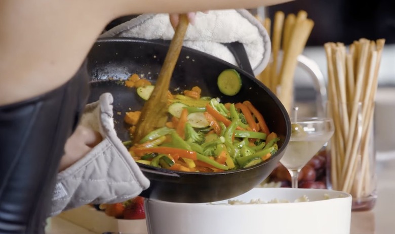 Kylie Jenner sliding veggies off a skillet and into a bowl full of pasta