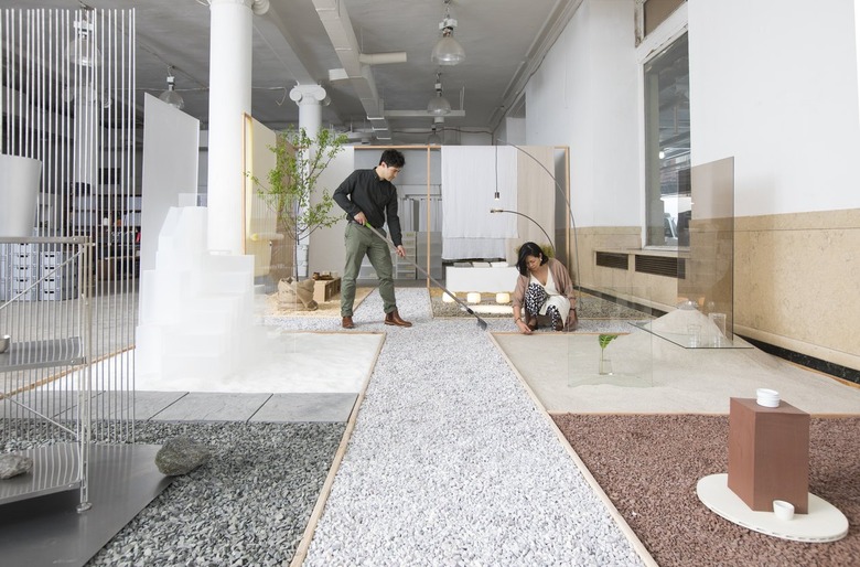 A dark-haired man and woman in a large open white studio space with different colored rocks and materials sectioned off on the floor.