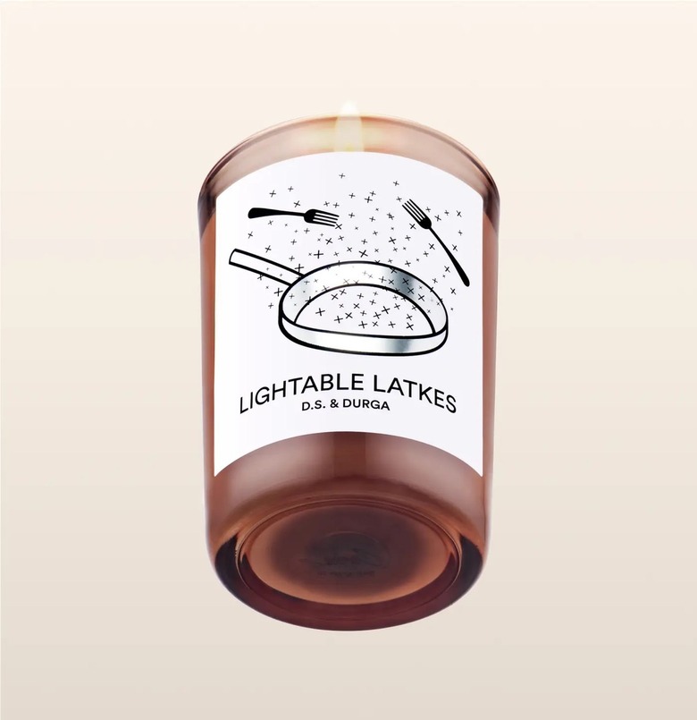 D.S. & Durga's Lightable Latkes candle in a transparent brown jar with an illustration of a frying pan and two forks on it.