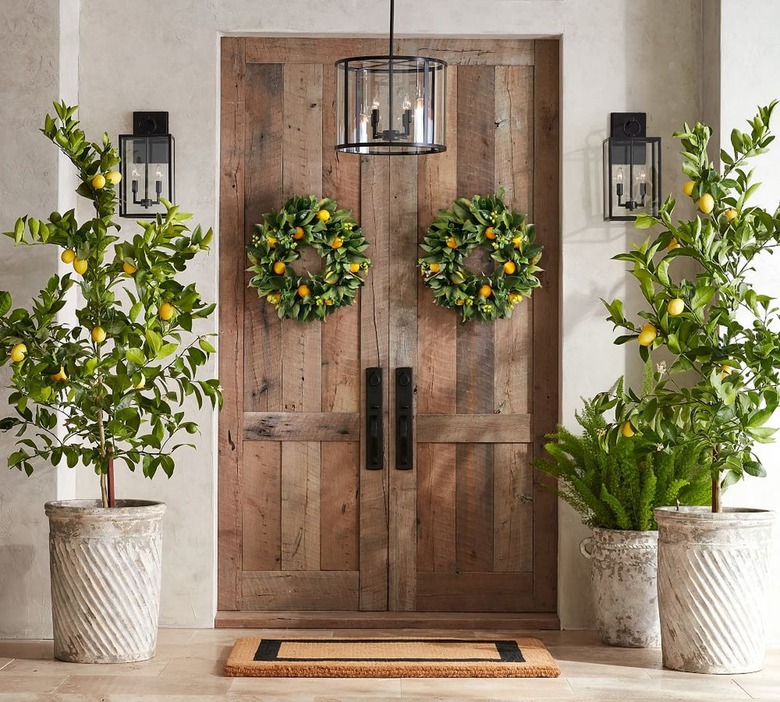 Image of double wooden front doors with faux lemon and magnolia wreaths on either side. There are planters with lemon trees on either side of the doorway