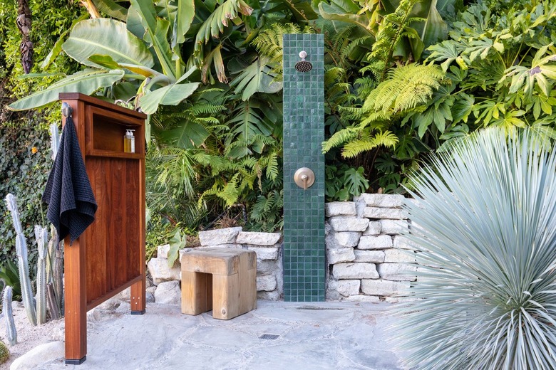 outdoor shower framed by lush foliage and a stone wall