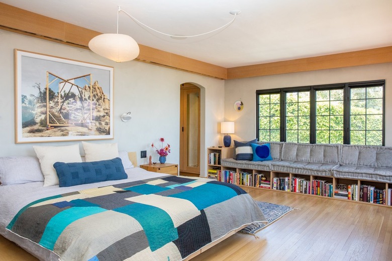 primary bedroom with blue quilt and wall of windows with bench seating