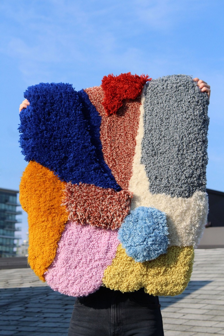 Multicolored patterned rug being held by two hands outside with blue sky in the background
