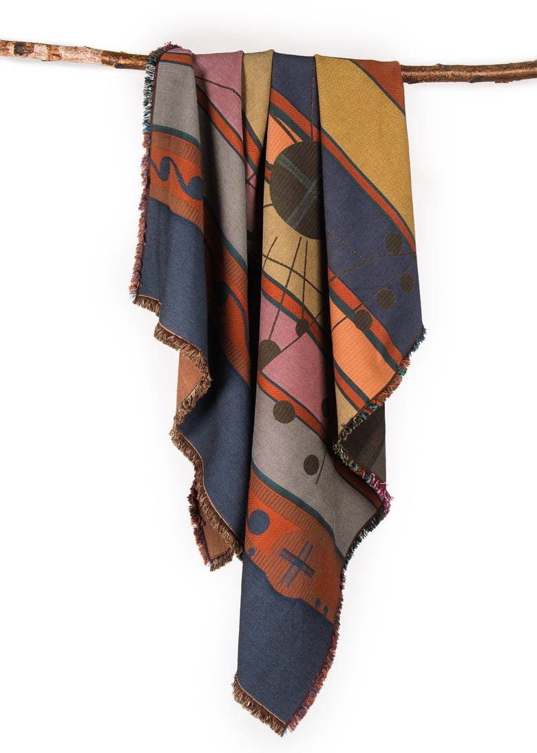 A colorful woven blanket hanging from a wooden rod on a white background.