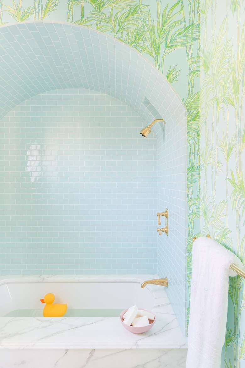 A white marble tub with a light blue backsplash and bamboo wallpaper.
