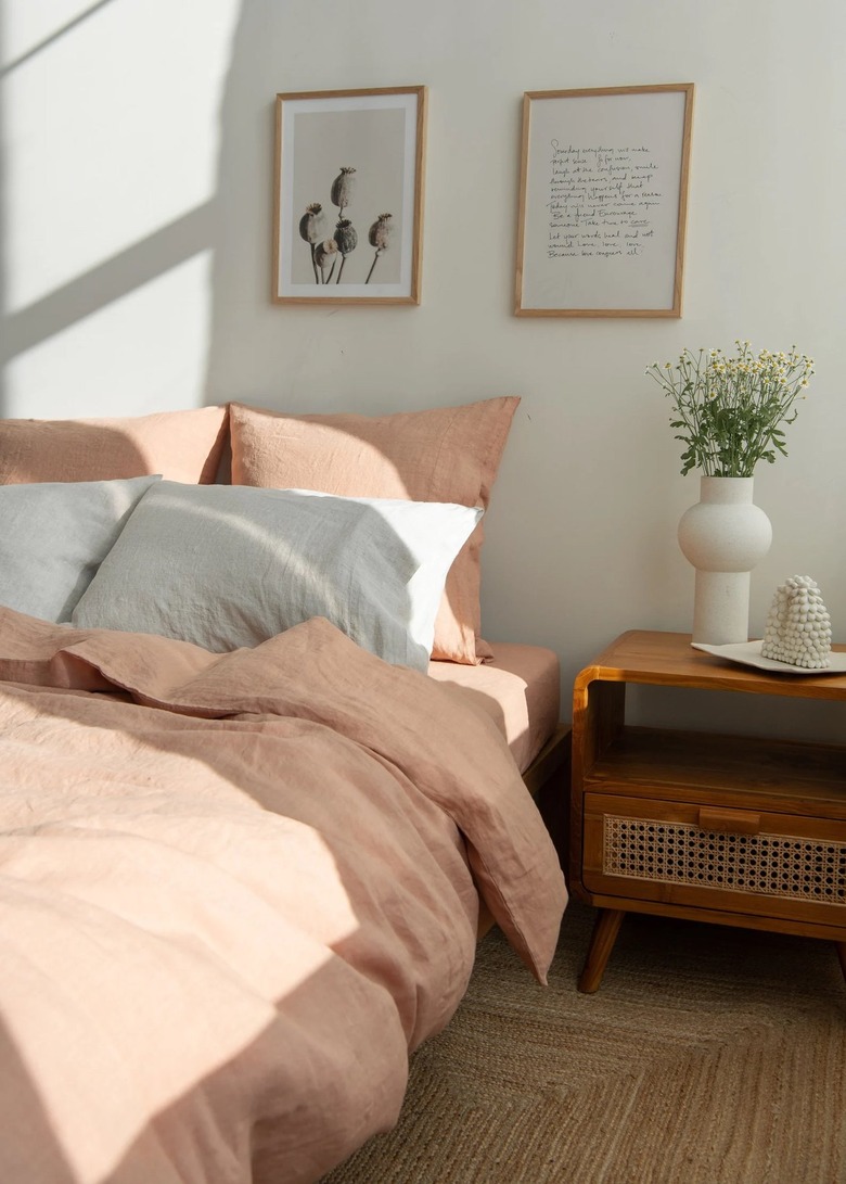 Light clay begging on a bed next to a nightstand and in front of a wall with two framed black and white prints.