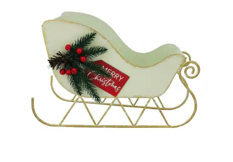 A decorative white sleigh with gold trim. A sprig of red berries and pine is on the side of the sleigh