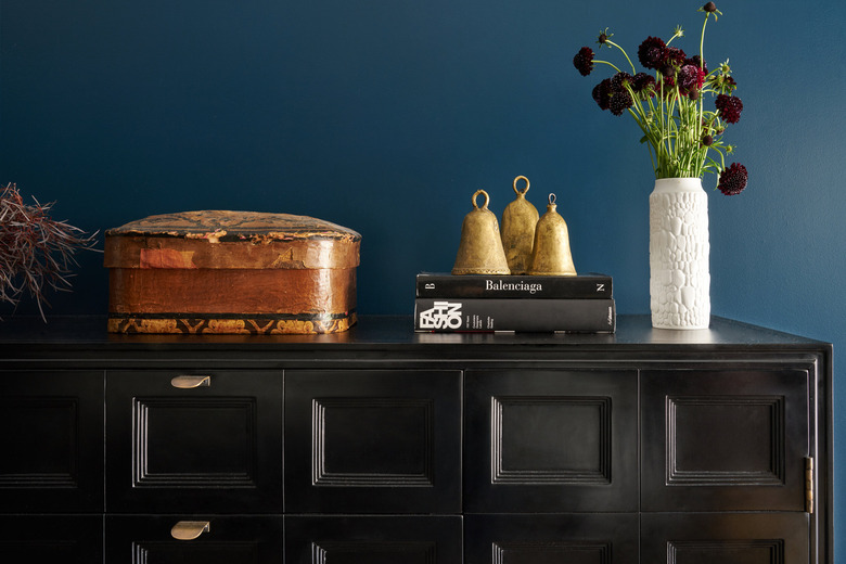 Minimalist entryway design with black cabinet with gold hardware against turquoise wall.