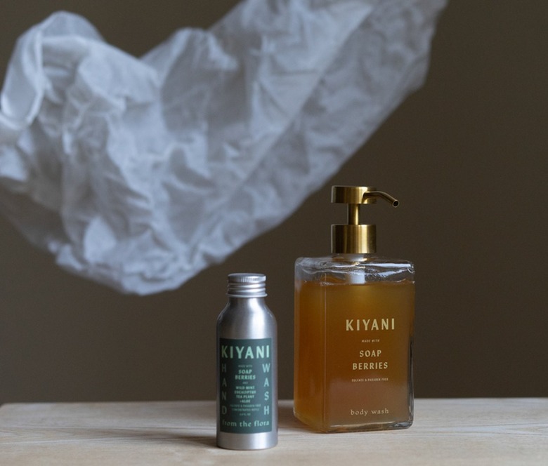 Kiyani's aluminum bottle of soap berry soap concentrate next to a glass dispenser filled with the soap mixed with water.